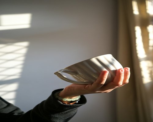 A relaxed person sitting near a bright window holding a warm porcelain cup with soft shadows around