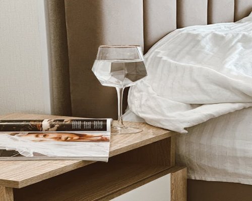 A clean crystal glass of mineral water standing on a wooden nightstand in a naturally lit bedroom