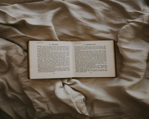 An open paperback book resting gently on soft beige linen sheets ready for peaceful bedtime reading